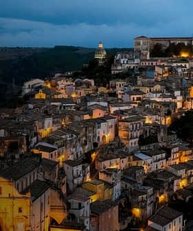 Luchtfoto van een historische Italiaanse stad die 's avonds verlicht is, met zichtbare gebouwen en straten. Olive Oil Times