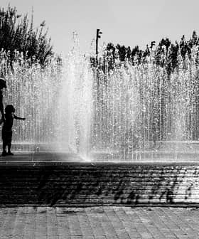 Силуэты детей, играющих в фонтане, на заднем плане - брызги воды. Olive Oil Times