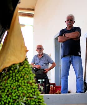 4 人の男性が屋内でオリーブの抽出工程を観察しています。 - Olive Oil Times