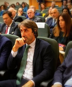 Grupa pojedinaca sjedi u konferencijskom okruženju, neki nose slušalice i sudjeluju u raspravi. - Olive Oil Times