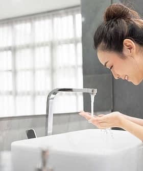 Una mujer con una bata blanca se lava las manos en un lavabo moderno con agua corriente. Olive Oil Times