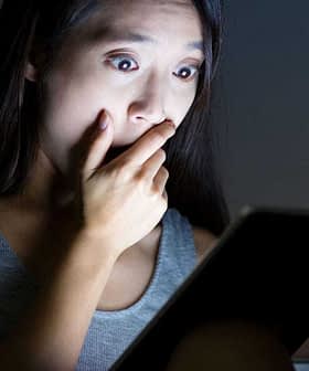 Una donna con i capelli lunghi che sembra scioccata mentre tiene in mano un tablet in una stanza scarsamente illuminata. - Olive Oil Times