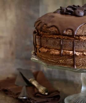 Bolo de chocolate coberto com ganache de chocolate e gotas de chocolate em um suporte de vidro para bolos. - Olive Oil Times