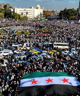 Ένα μεγάλο πλήθος συγκεντρώθηκε σε μια δημόσια πλατεία κρατώντας μια συριακή σημαία με τρία αστέρια. - Olive Oil Times