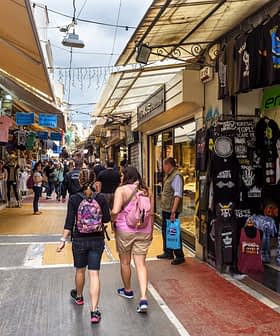 Dos personas caminando por una calle de mercado llena de tiendas y puestos que venden diversos artículos. Olive Oil Times