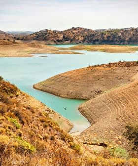 Una vista de un embalse con una costa seca y colinas circundantes en un paisaje natural. Olive Oil Times