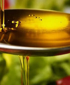 Krupni plan srebrne žlice koja drži maslinovo ulje iznad svježeg povrća na tanjuru. - Olive Oil Times