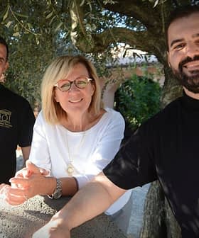 Tres personas juntas al aire libre, sonriendo y posando para una foto cerca de un olivo. Olive Oil Times