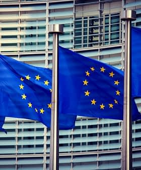 Чотири прапори Європейського Союзу на стовпах перед сучасною будівлею. - Olive Oil Times