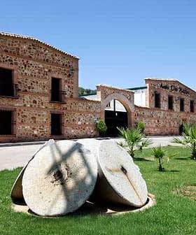 Vue extérieure d'un moulin à huile d'olive présentant de grandes meules en pierre au premier plan. - Olive Oil Times