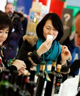 Dvije žene kušaju maslinovo ulje na sajmu, jedna drži šalicu za degustaciju, a druga promatra. - Olive Oil Times