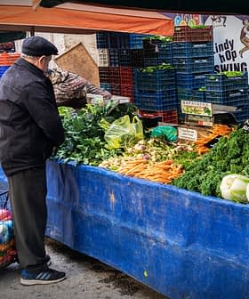 Man bekijkt verse groenten op een marktkraam waar verschillende producten zijn uitgestald. Olive Oil Times