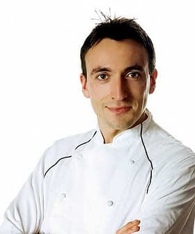 Een chef-kok in een wit uniform, met gekruiste armen, kijkt recht in de camera. Olive Oil Times