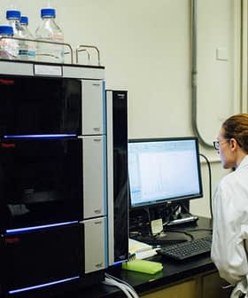 Laboratorijski tehnik v beli halji upravlja analitično opremo in pregleduje podatke na računalniškem zaslonu. - Olive Oil Times
