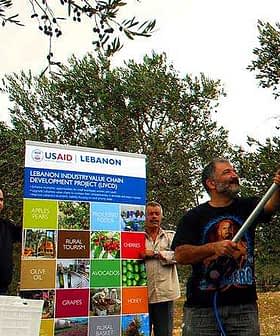 Arka planda bir pankartla USAID Lübnan Sanayi Değer Zinciri Geliştirme Projesi'ne katılan üç adam. - Olive Oil Times
