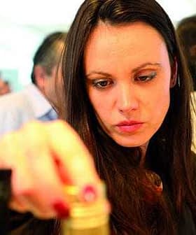 Femme aux cheveux longs examinant une bouteille dans un contexte social, se concentrant intensément sur l'objet. - Olive Oil Times