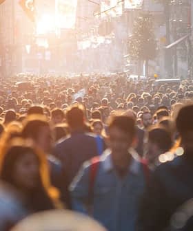 日落时分，阳光透过缝隙照射下来，一大群人走在繁忙的城市街道上。 - Olive Oil Times