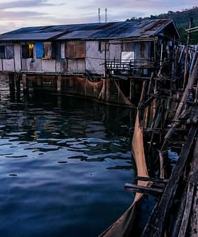 Maisons sur pilotis en bois construites sur l'eau avec une passerelle en bois menant à elles au crépuscule. - Olive Oil Times
