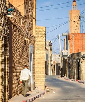Rua estreita ladeada por prédios de tijolos em uma vila, com uma pessoa caminhando ao lado. Olive Oil Times