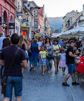 Multidão de pessoas caminhando por uma rua com mesas ao ar livre e lojas em uma cidade. - Olive Oil Times