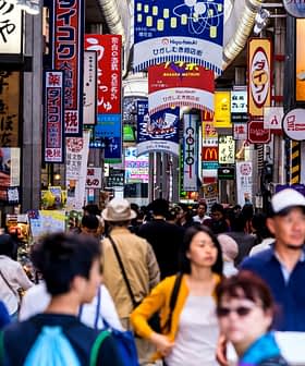 Folla di persone che camminano in un vivace mercato di strada pieno di cartelli colorati in Giappone. - Olive Oil Times