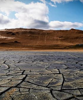 Surface de terre sèche et craquelée avec un fond montagneux sous un ciel nuageux. - Olive Oil Times