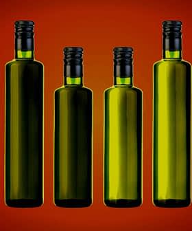 Osem steklenic iz zelenega stekla s črnimi pokrovčki, razporejenih v vrsti na prelivajočem se ozadju. - Olive Oil Times