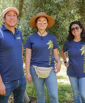 Cinque individui che indossano magliette abbinate stanno in piedi insieme al centro di un ulivo. - Olive Oil Times