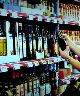Una mujer examina una botella de aceite de oliva mientras compra en un pasillo de un supermercado lleno de diversos aceites. Olive Oil Times