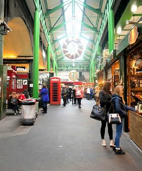 Interior view of a market featuring various stalls and shoppers walking through the aisles. - Olive Oil Times