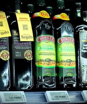 Différentes bouteilles d'huile d'olive exposées sur une étagère de magasin avec des étiquettes et des informations sur les prix. - Olive Oil Times