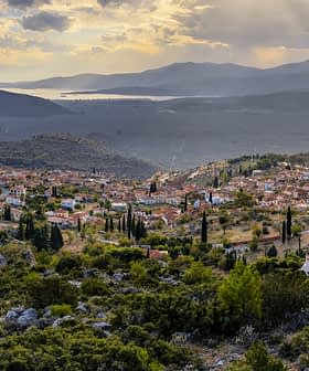 Una vista panoramica di un villaggio incastonato tra le montagne con il verde circostante e le colline sullo sfondo. - Olive Oil Times