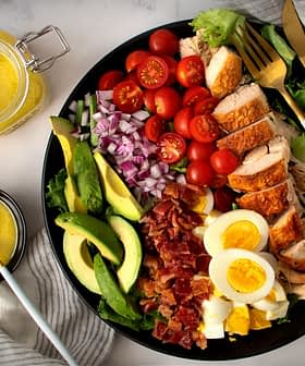Izgara tavuk, avokado, cherry domates ve haşlanmış yumurtadan oluşan, siyah bir tabakta servis edilen rengarenk bir salata. Olive Oil Times