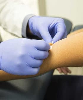 Un profesional médico que usa guantes aplica un vendaje en el brazo de un paciente en un entorno clínico. Olive Oil Times