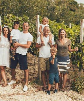 Grupa ljudi zajedno pozira u vinogradu s vinovom lozom u pozadini. - Olive Oil Times