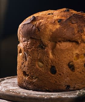 Una pagnotta rotonda con una crosta dorata e uvetta visibile su una superficie di legno. - Olive Oil Times