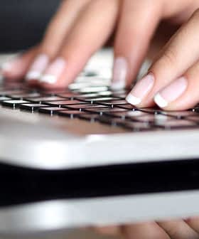 Primo piano di mani che digitano sulla tastiera di un computer portatile con superficie riflettente. - Olive Oil Times