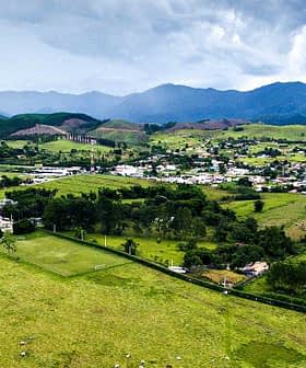 Vue aérienne d'une zone rurale avec des champs verts, une petite ville et des montagnes en arrière-plan. - Olive Oil Times