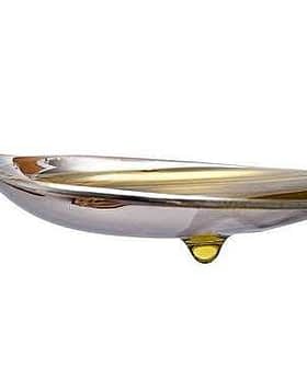 Una cuchara de plata con una gota de aceite de oliva en la punta de la cuchara. Olive Oil Times