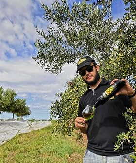 Man in sunglasses pouring olive oil from a bottle into a glass in an olive grove. - Olive Oil Times