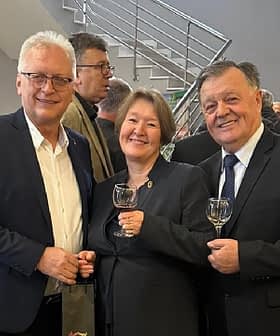 Tres personas juntas, cada una sosteniendo un vaso, en una reunión o evento. Olive Oil Times