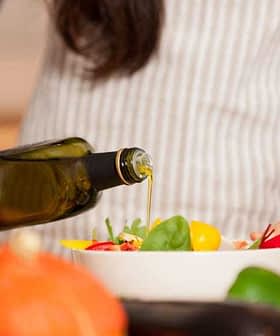 Persona que vierte aceite de oliva de una botella en una ensaladera llena de verduras. - Olive Oil Times