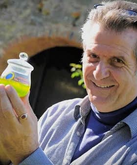 Un homme souriant tout en tenant un petit pot d'huile d'olive verte dans sa main. - Olive Oil Times