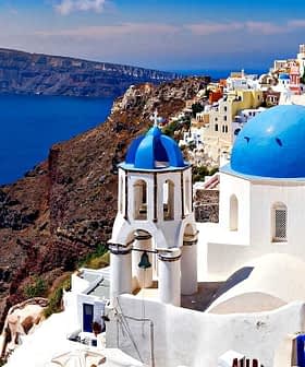 Vista de la isla de Santorini con edificios blancos con cúpulas azules contra el mar. Olive Oil Times