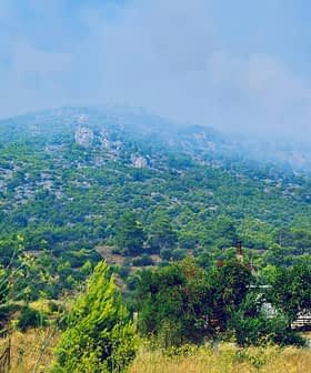 Uma área montanhosa coberta de vegetação verde e formações rochosas sob um céu azul com nuvens. - Olive Oil Times