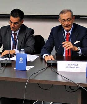 Τέσσερις ομιλητές κάθονται σε ένα τραπέζι κατά τη διάρκεια μιας συζήτησης, με μικρόφωνα και κάρτες ονομάτων μπροστά τους. - Olive Oil Times