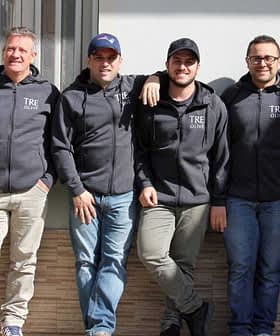 「TRE Olive」とプリントされた灰色のパーカーを着た6人の男性が一列に並んで立っています。 - Olive Oil Times