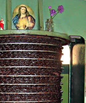 Máquina prensadora de aceite de oliva con un icono religioso y flores encima. - Olive Oil Times