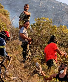 Bombeiros e voluntários trabalhando juntos para controlar um incêndio florestal em uma área montanhosa com vegetação. - Olive Oil Times