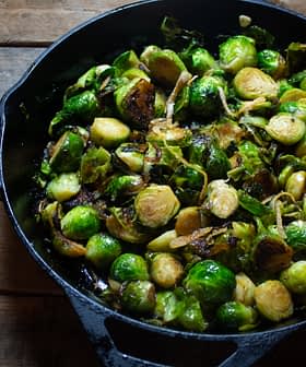 Sautéed Brussels sprouts with caramelized onions in a cast iron skillet on a wooden surface. - Olive Oil Times